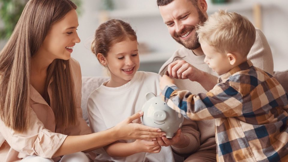 Família sorrindo enquanto criança deposita moeda em um cofrinho