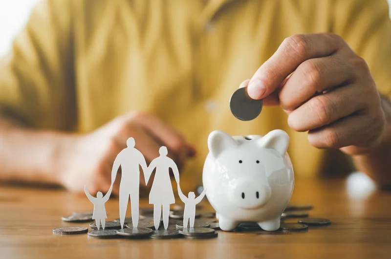 Família de papel ao lado de um cofrinho, com uma moeda sendo depositada